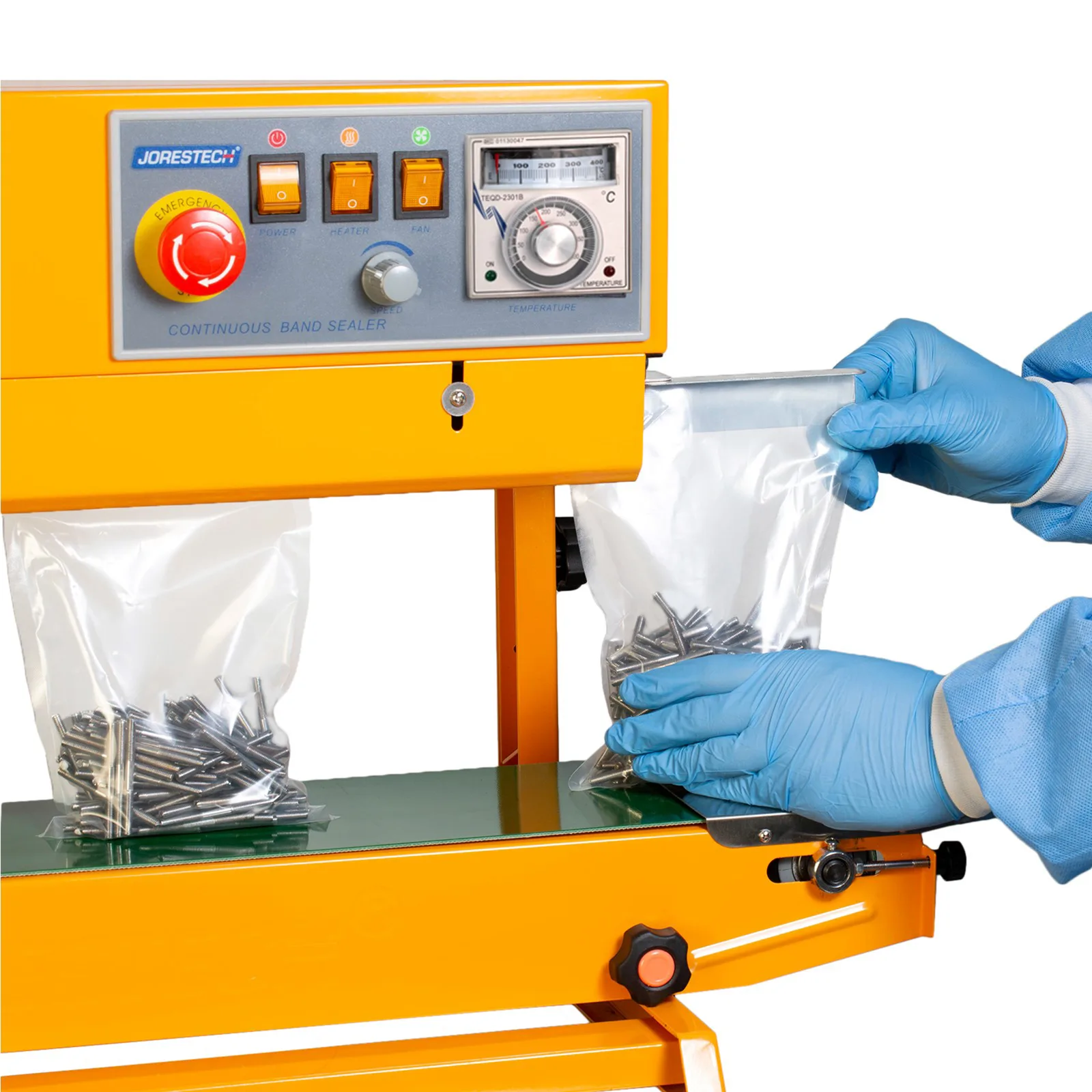 Trabajador con equipo de protección personal introduciendo bolsas de plástico llenas de clavos en la selladora continua de bolsas con calor JORES TECHNOLOGIES® amarilla. La selladora de bolsas está colocada para aplicaciones verticales