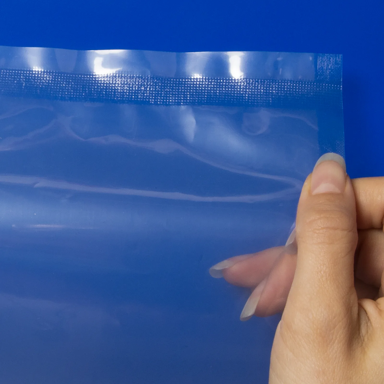 primer plano de la mano de una persona sosteniendo una bolsa de plástico sellada por una selladora continua de banda JORES TECHNOLOGIES® sobre un fondo azul. El detalle muestra el patrón del sellado.