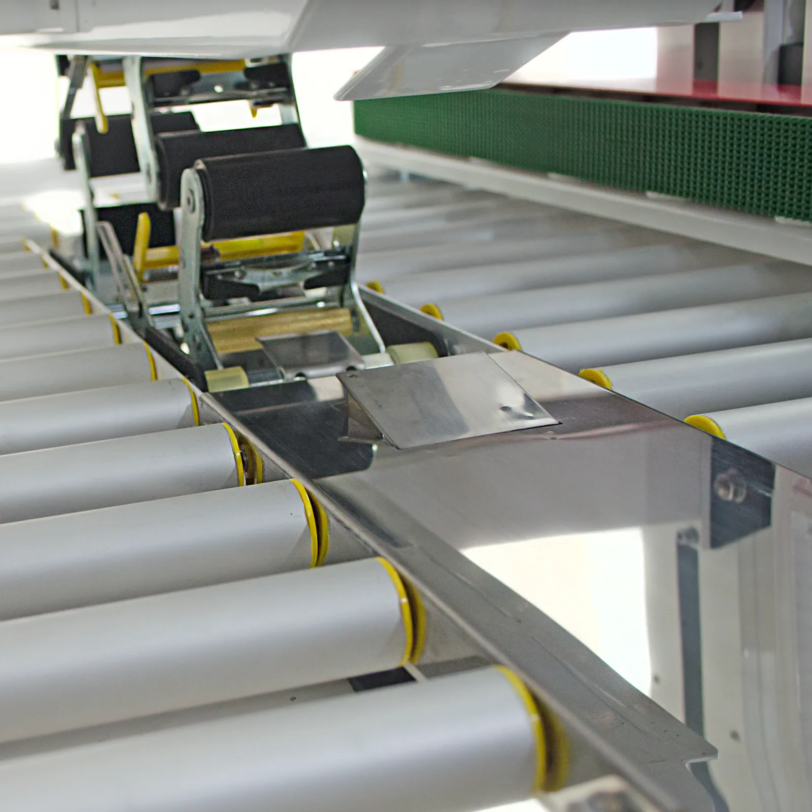 barras rodantes de metal plateado y bandas de tracción verdes en una máquina selladora de cajas con tracción lateral