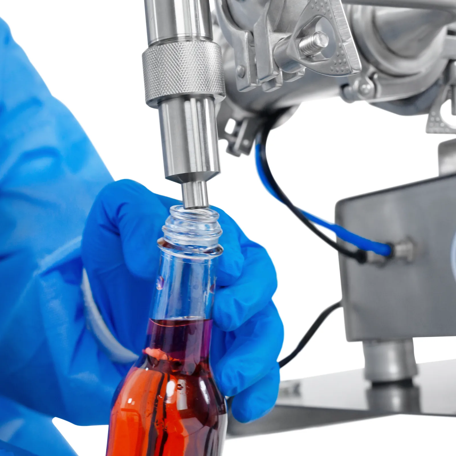 Trabajador con guantes de seguridad de nitrilo operando el pistón dosificador de baja viscosidad JORES TECHNOLOGIES®. La persona está colocando una botella de 250 ml debajo de la punta de la boquilla antigoteo para llenarla con precisión mediante la máquina llenadora de líquidos.