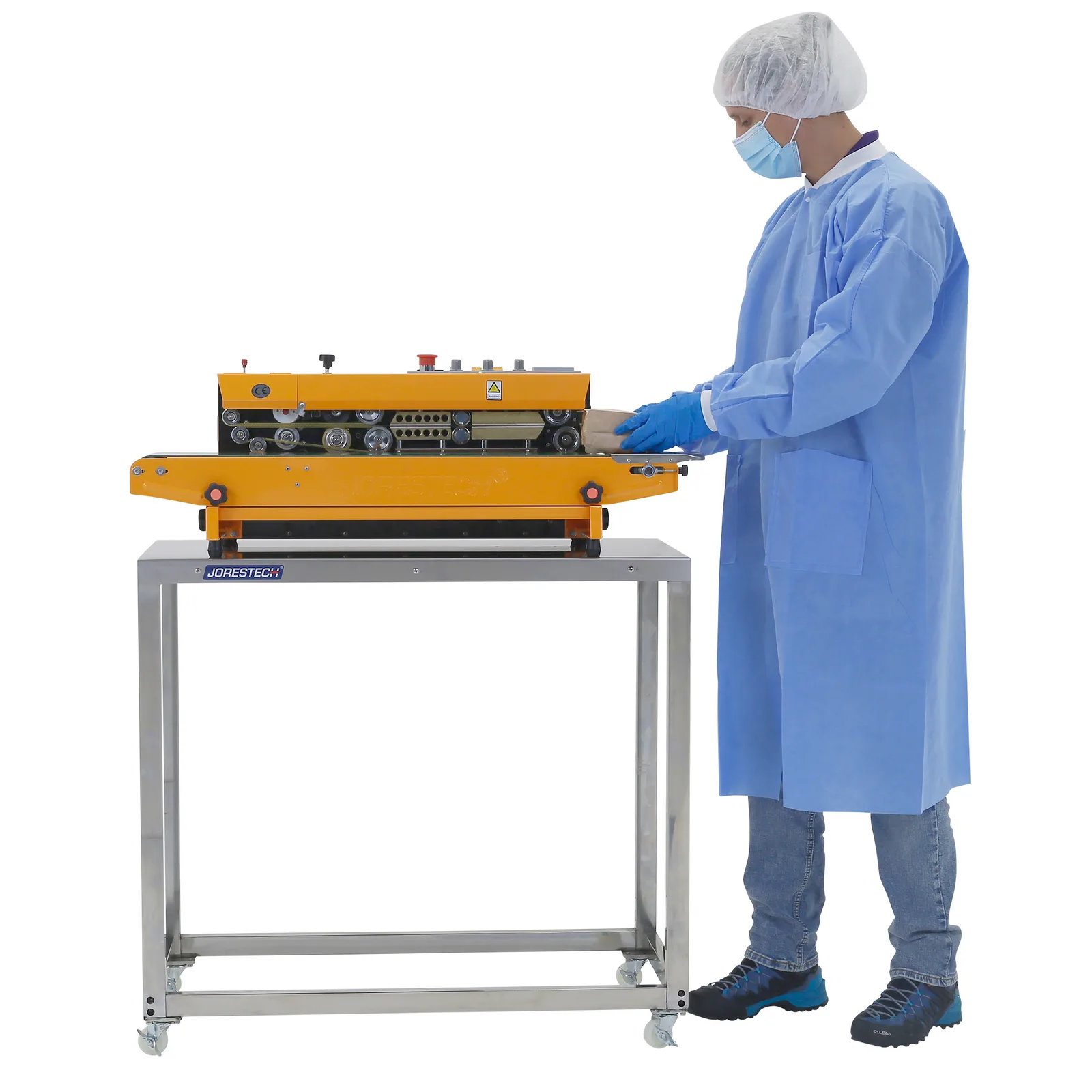 Una persona que lleva EPI desechable y guantes de nitrilo utilizando una selladora continua de banda, colocada sobre una mesa de preparación de acero inoxidable JORES TECHNOLOGIES®