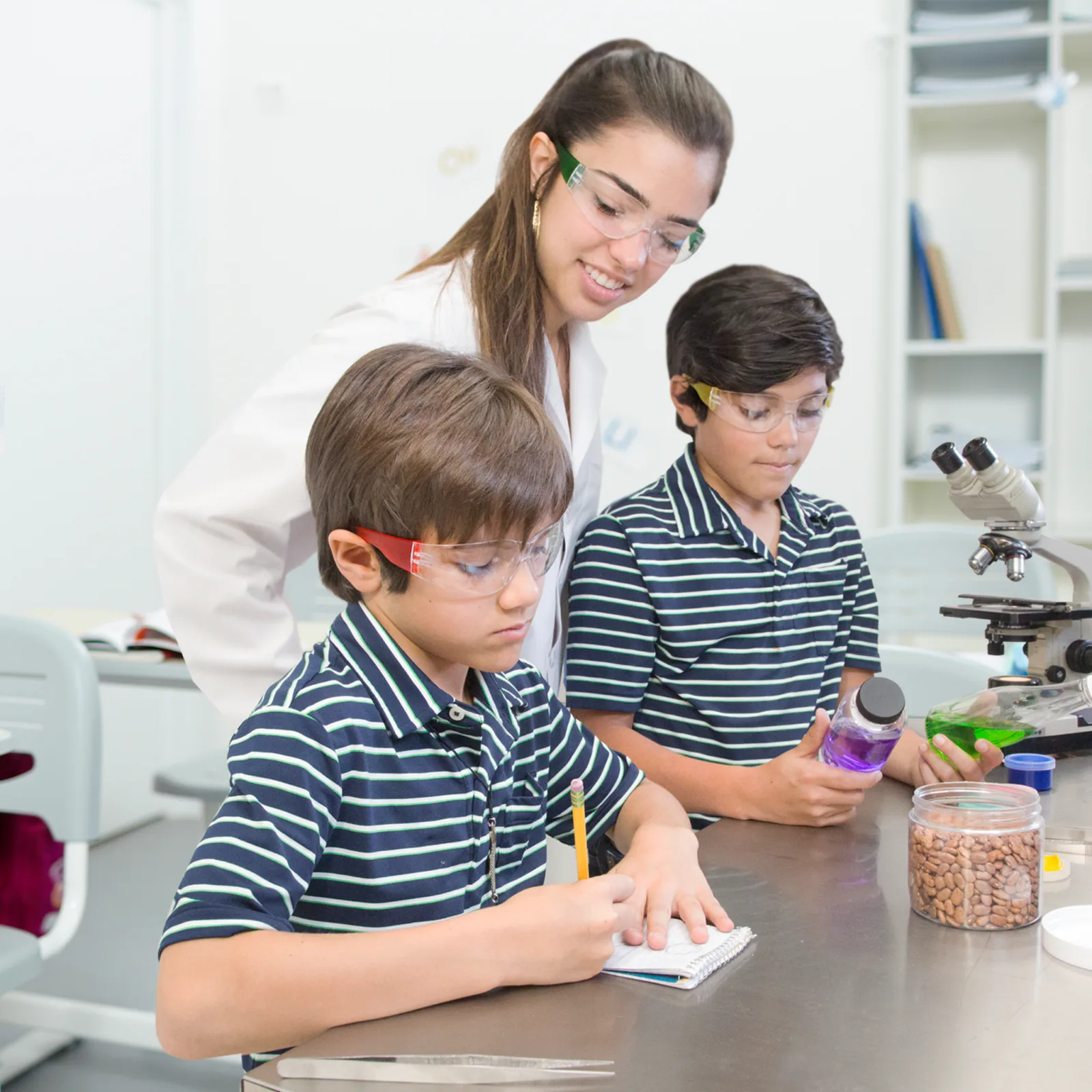 2 niños con uniforme y su profesora en un laboratorio escolar usando gafas de seguridad de alto impacto multicolor JORESTECH