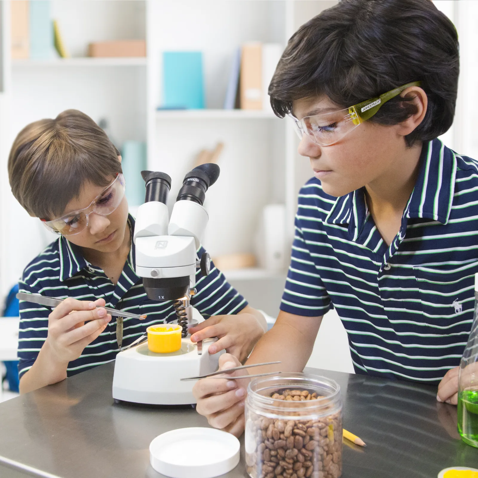 Dos niños llevan gafas de seguridad JORESTECH mientras operan un microscopio en el laboratorio de la escuela