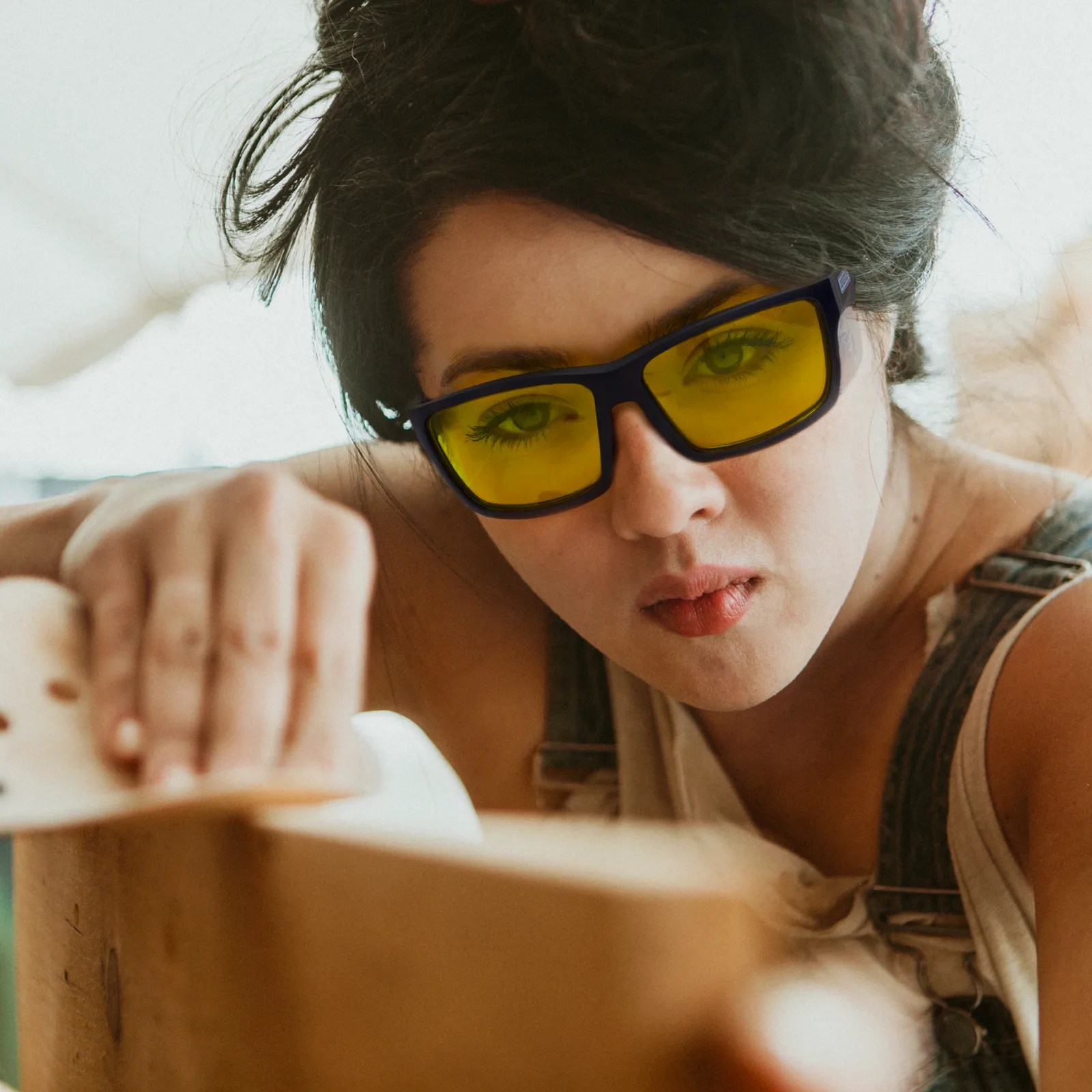 Imagen de una mujer que lleva las gafas de seguridad amarillas JORESTECH con protectores laterales para protección contra impactos fuertes mientras esculpe una gran pieza de madera en un proyecto de bricolaje